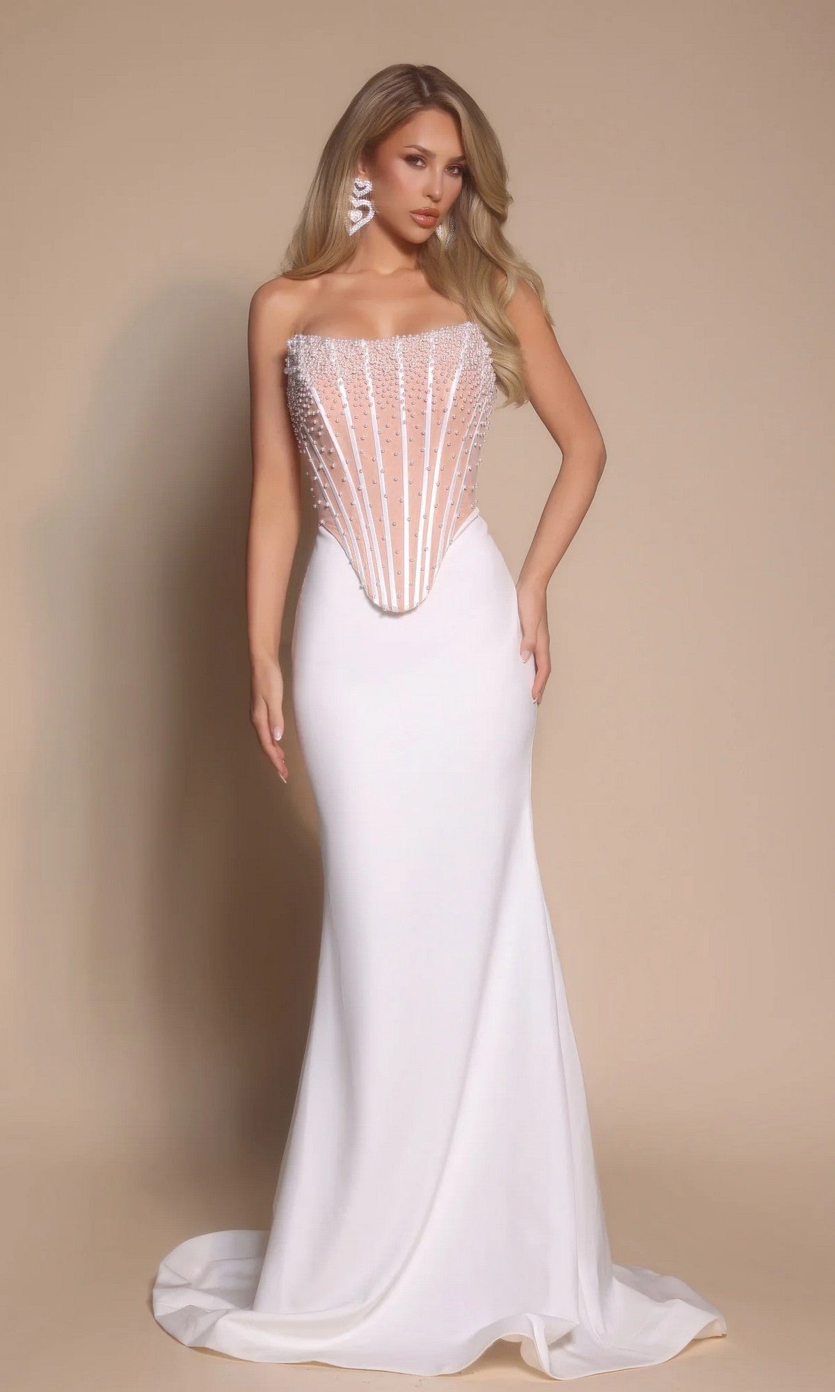 A woman wears the Portia and Scarlett PS26008 long formal dress in ivory, featuring a strapless beaded corset bodice and floor-length skirt, standing against a plain beige background.
